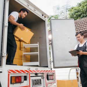 Uniformed removal company workers unload boxes and furniture from the truck exhibiting excellent teamwork. Their dedication guarantees a smooth move into the new home ensuring happiness. Moving Day